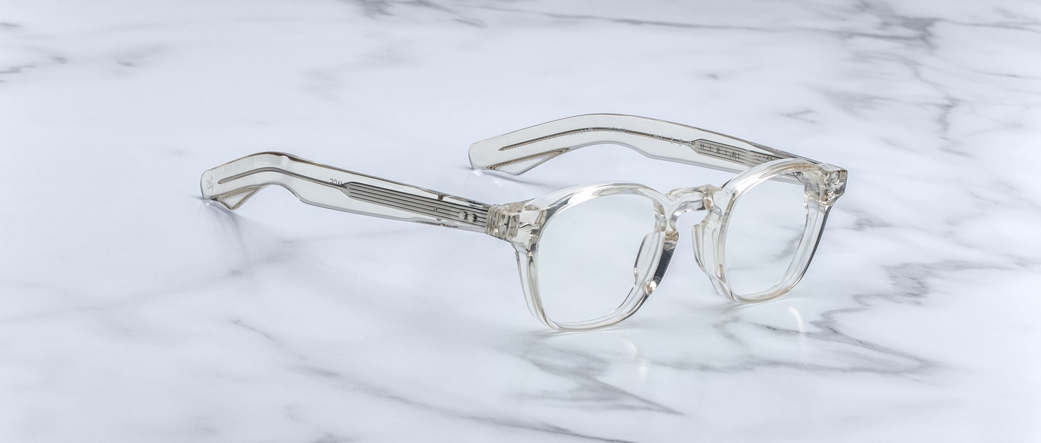 The Jacques Marie Mage Zephirin features handcrafted clear acetate with rectangular lenses and wide arms, displayed on white marble—a refined, limited edition spectacle from Jacques Marie Mage.