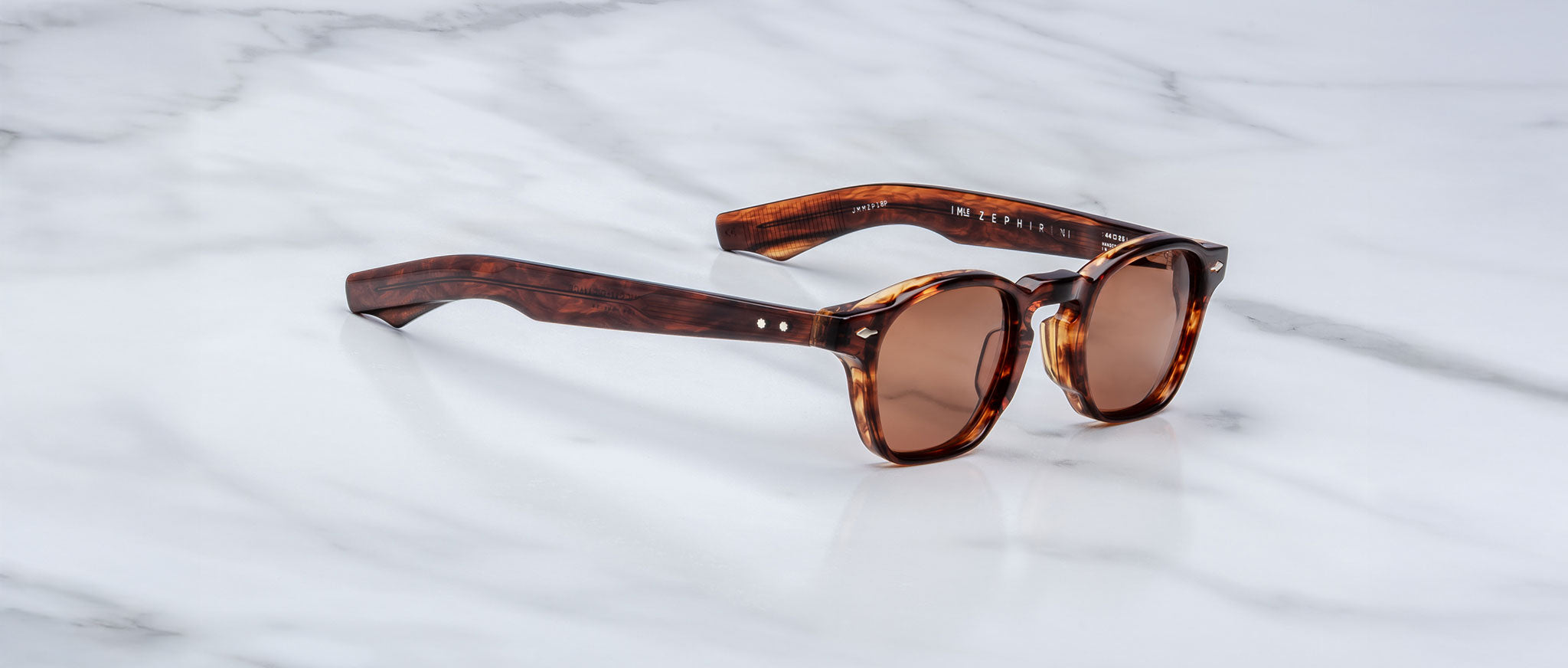 A handcrafted pair of Jacques Marie Mage Zephirin sunglasses featuring brown tortoiseshell acetate, round lenses, and thick frames, elegantly displayed on a white marble surface.