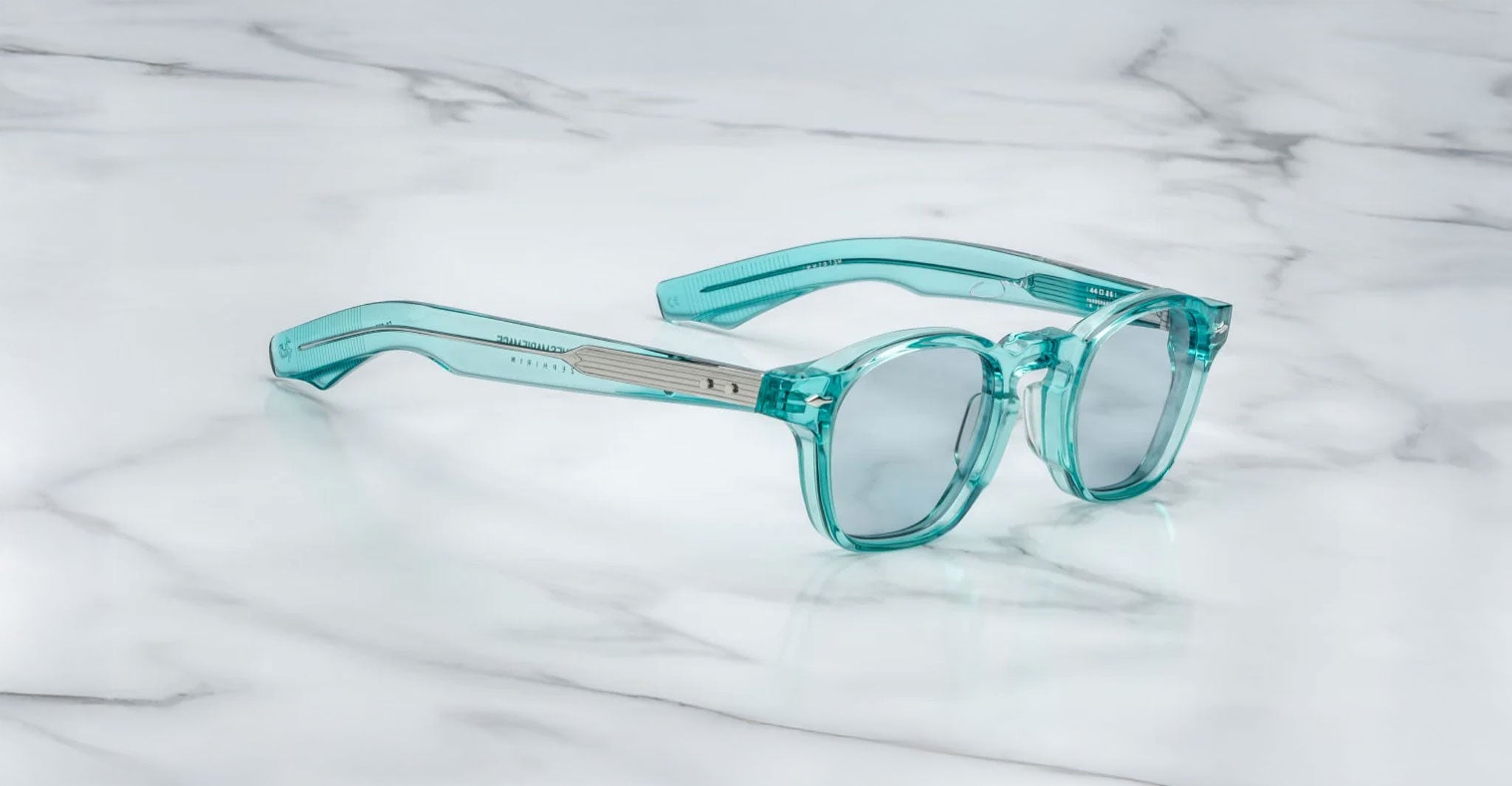 The Jacques Marie Mage Zephirin by Jacques Marie Mage features handcrafted acetate frames in transparent teal with round, thick lenses, elegantly displayed on white marble—a sophisticated limited edition eyewear piece.