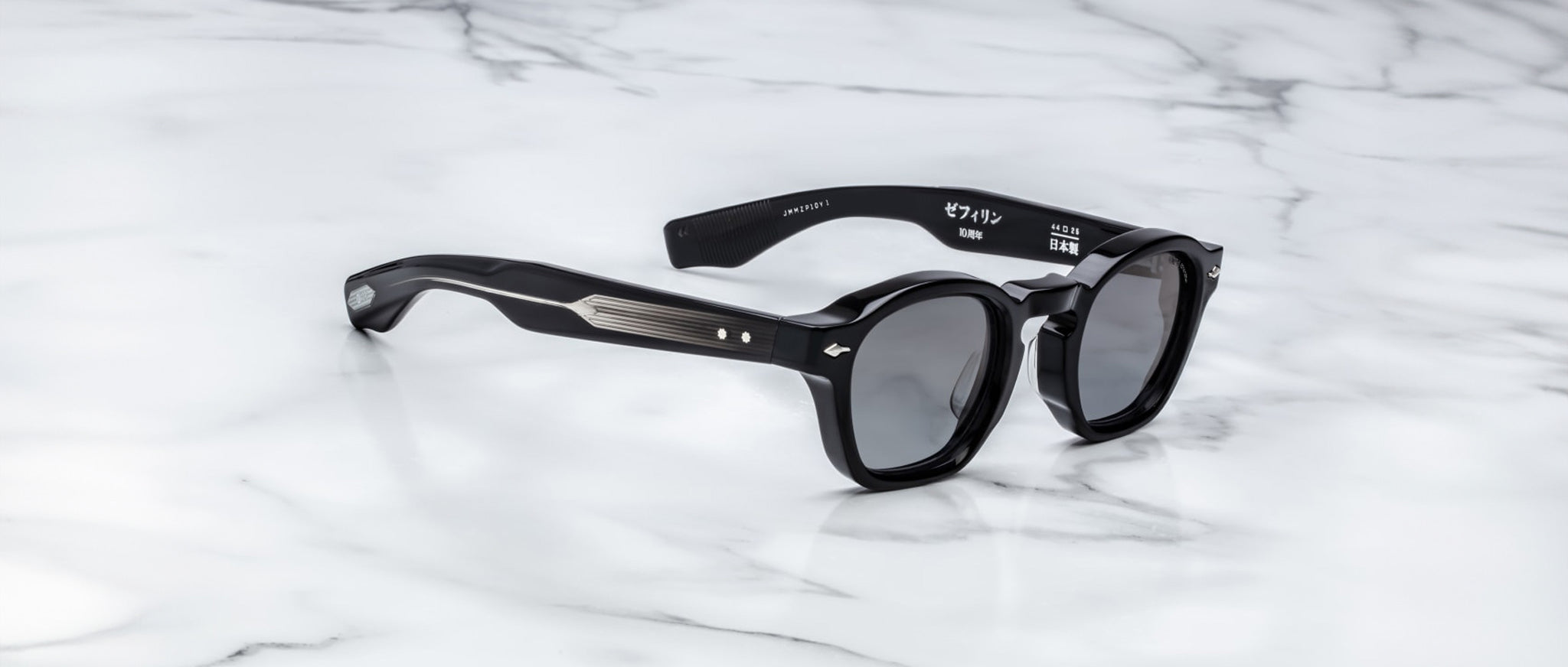 The Jacques Marie Mage Zephirin sunglasses by Jacques Marie Mage feature black round frames with silver temple accents, inspired by limited edition eyewear, displayed on a white marble surface.