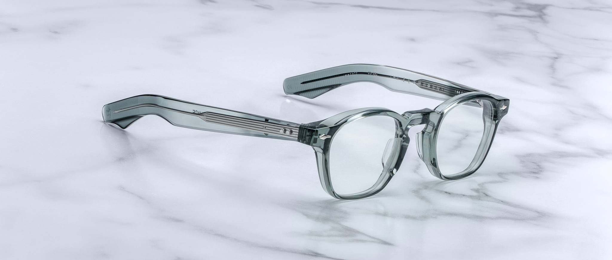 The Jacques Marie Mage Zephirin, handcrafted acetate spectacles with round lenses and thick arms, rest on a white marble surface—a refined piece from the exclusive Jacques Marie Mage collection.