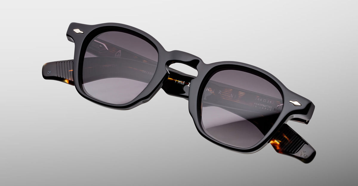 Jacques Marie Mage Zephirin sunglasses in Noir 11, angled front detail with glossy black acetate, gray-tinted lenses, and subtle tortoiseshell accents.