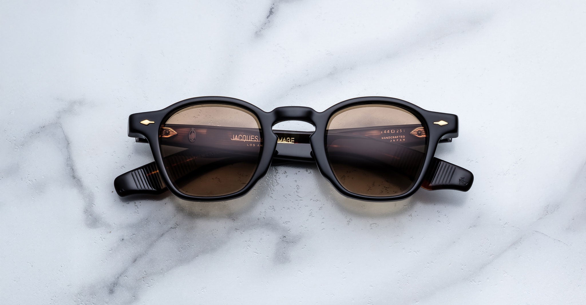 Jacques Marie Mage Zephirin in Noir 15 black round sunglasses with brown tinted lenses, top view, shown on white marble.