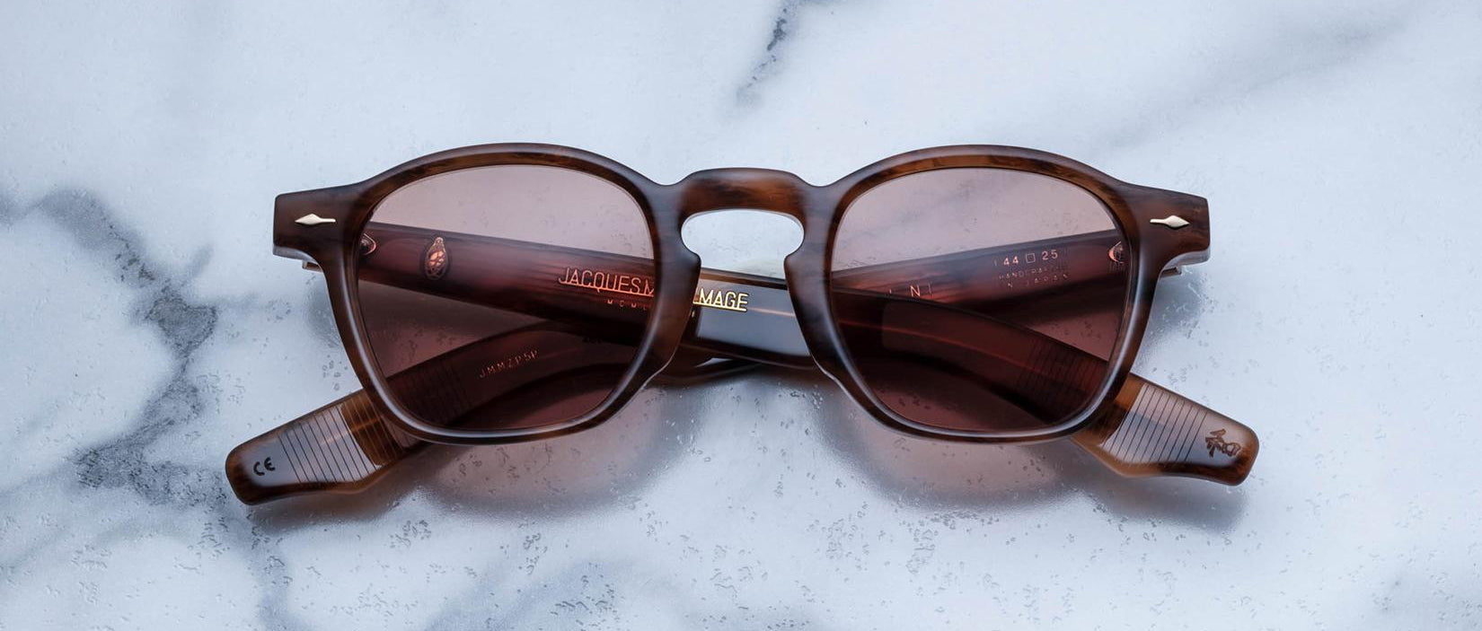 A pair of Jacques Marie Mage Zephirin brown square-framed sunglasses with tinted lenses rests on white marble, highlighting the sophistication of this limited edition eyewear.