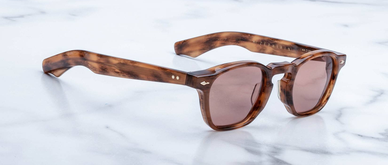 The limited edition Jacques Marie Mage Zephirin sunglasses feature round brown lenses and thick tortoiseshell acetate frames, handcrafted by Jacques Marie Mage and elegantly displayed on a white marble surface.