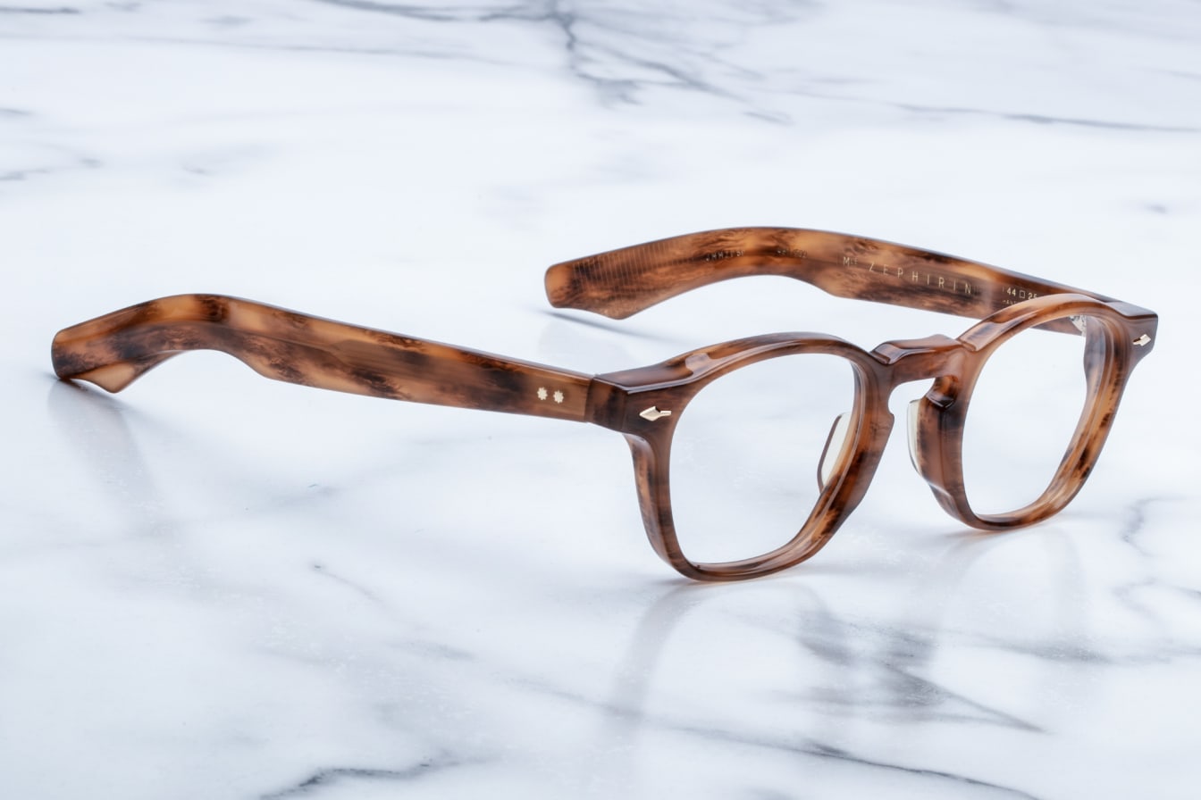 The Jacques Marie Mage Zephirin, handcrafted brown tortoiseshell acetate spectacles with round lenses, rests on a white marble surface.
