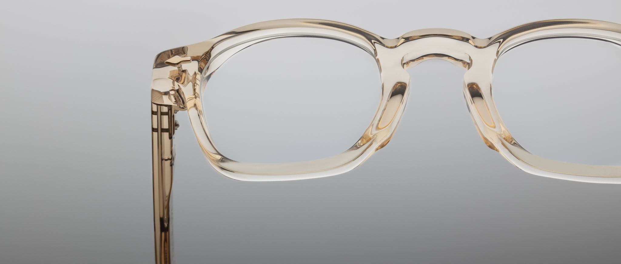 Close-up of the clear, thick-rimmed Jacques Marie Mage Zephirin frames in transparent beige, highlighting handcrafted acetate detail against a plain background.