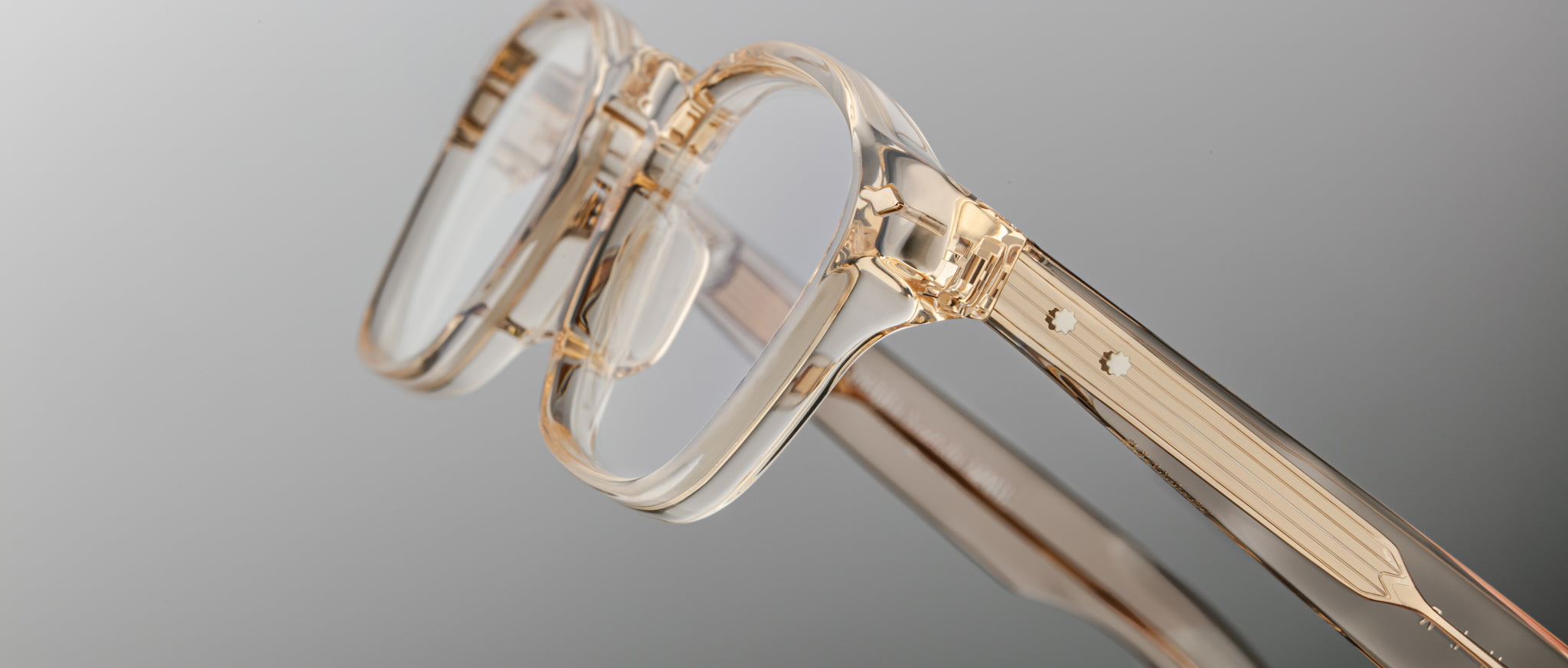 Close-up of Jacques Marie Mage Zephirin eyeglasses featuring transparent beige handcrafted acetate frames, rectangular lenses, and a minimalist design, set against a plain gradient background.