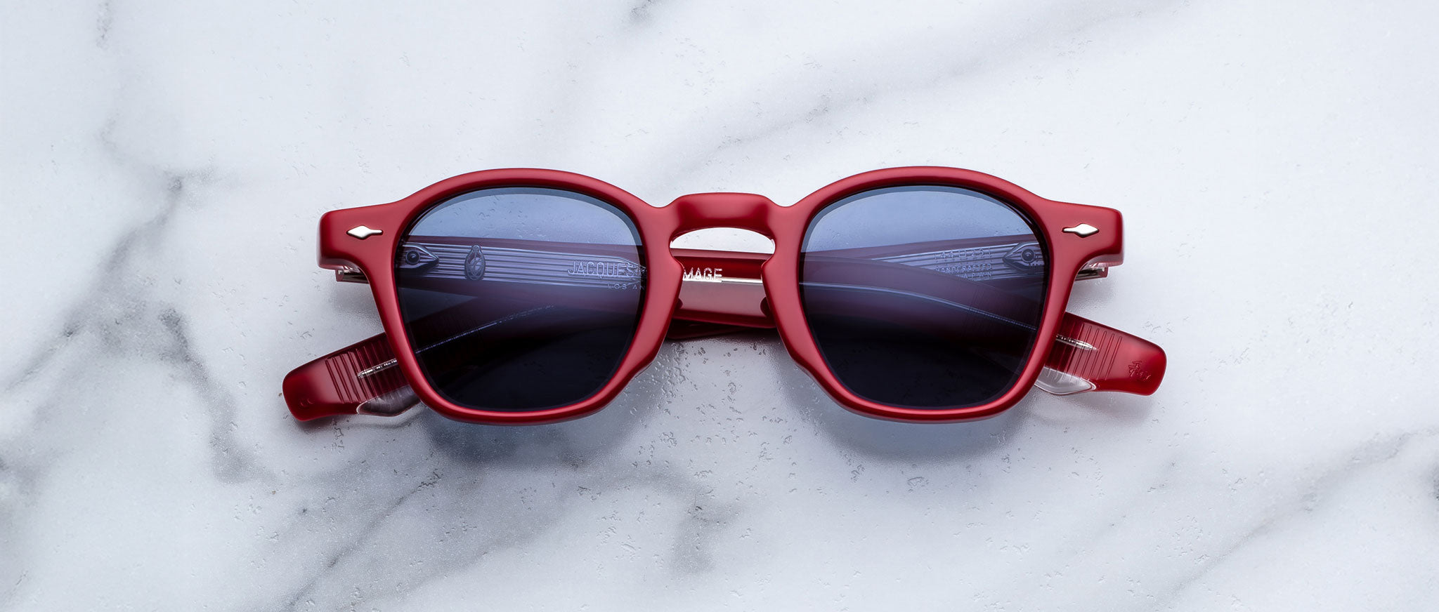 Jacques Marie Mage Zephirin in Pirate red sunglasses with dark lenses, viewed from above, shown on a flat surface.