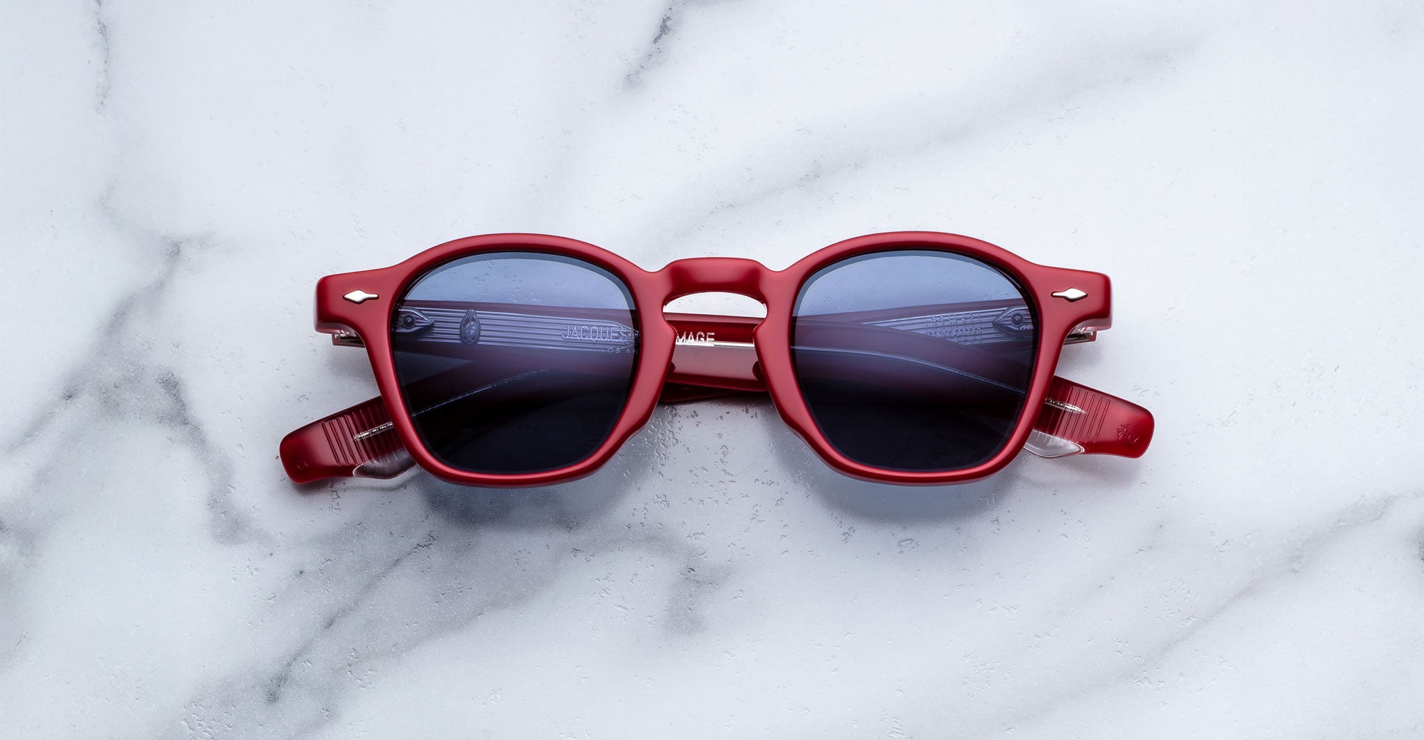 Jacques Marie Mage Zephirin in Pirate red sunglasses with dark lenses, viewed from above, shown on a flat surface.