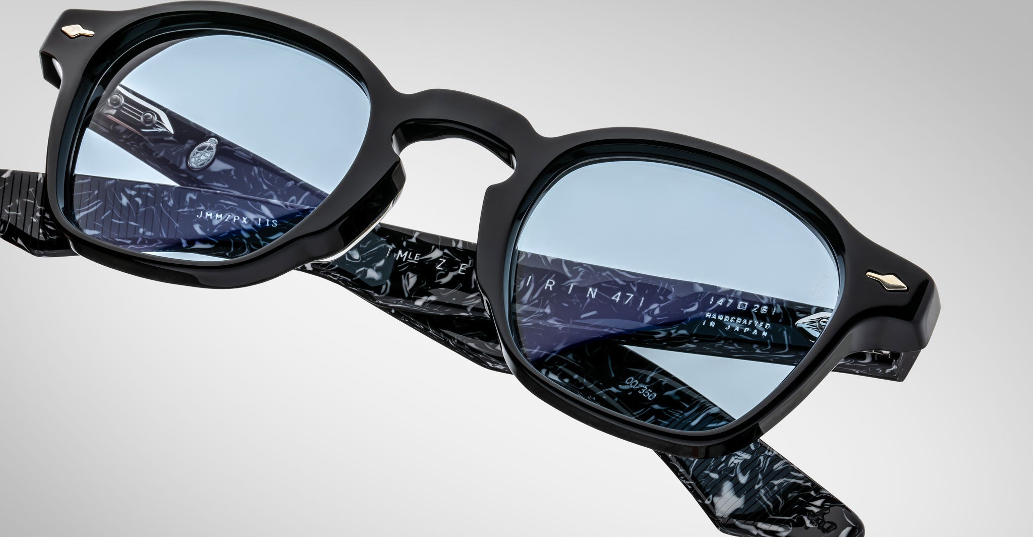 Close-up of Jacques Marie Mage Zephirin eyeglasses, featuring black frames, blue lenses, and patterned temples, crafted from premium handcrafted acetate and shown against a plain background.