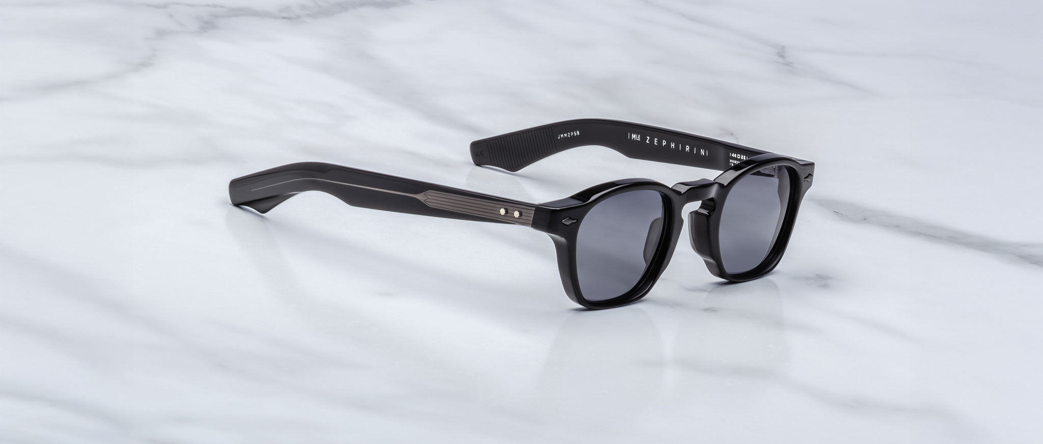 Jacques Marie Mage Zephirin sunglasses with round lenses and thick handcrafted acetate frames rest on a white marble surface, embodying the iconic style of Jacques Marie Mage.