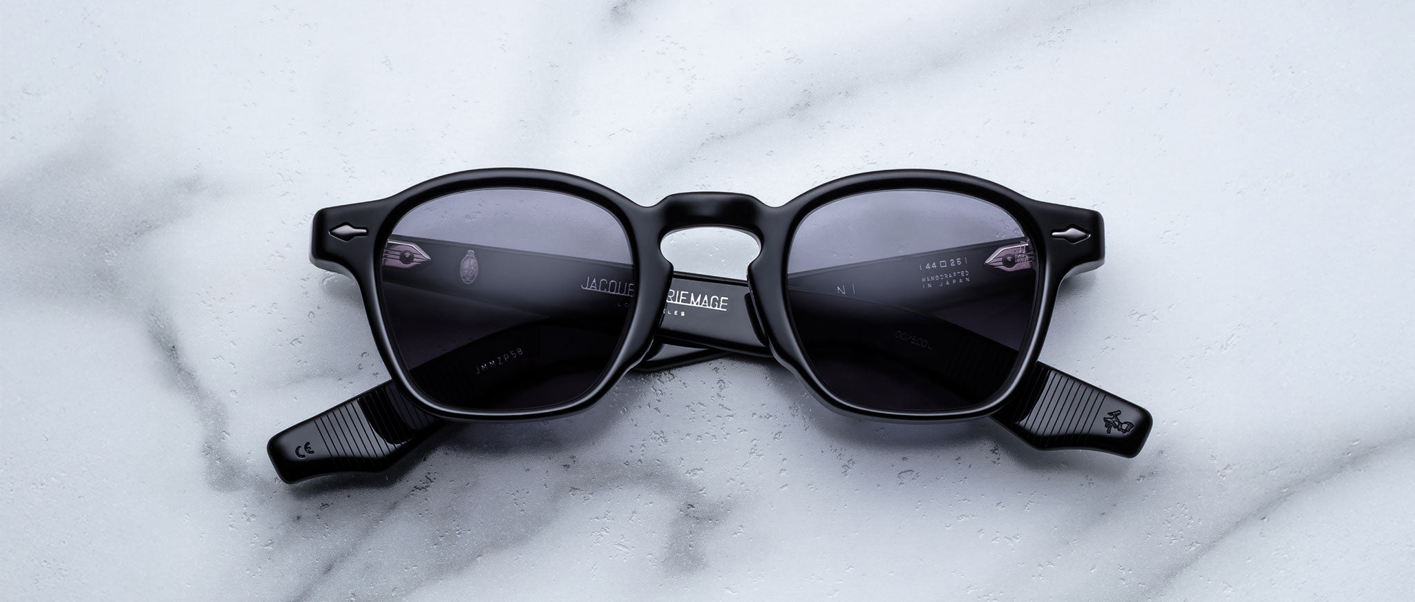 The Jacques Marie Mage Zephirin sunglasses, limited edition with black frames and dark lenses, are showcased on a white marble surface.