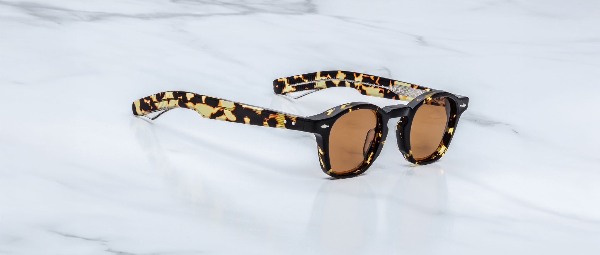 Jacques Marie Mage Zephirin sunglasses by Jacques Marie Mage, featuring tortoiseshell frames and brown lenses, rest on a white marble surface and highlight the exclusive charm of limited edition eyewear.