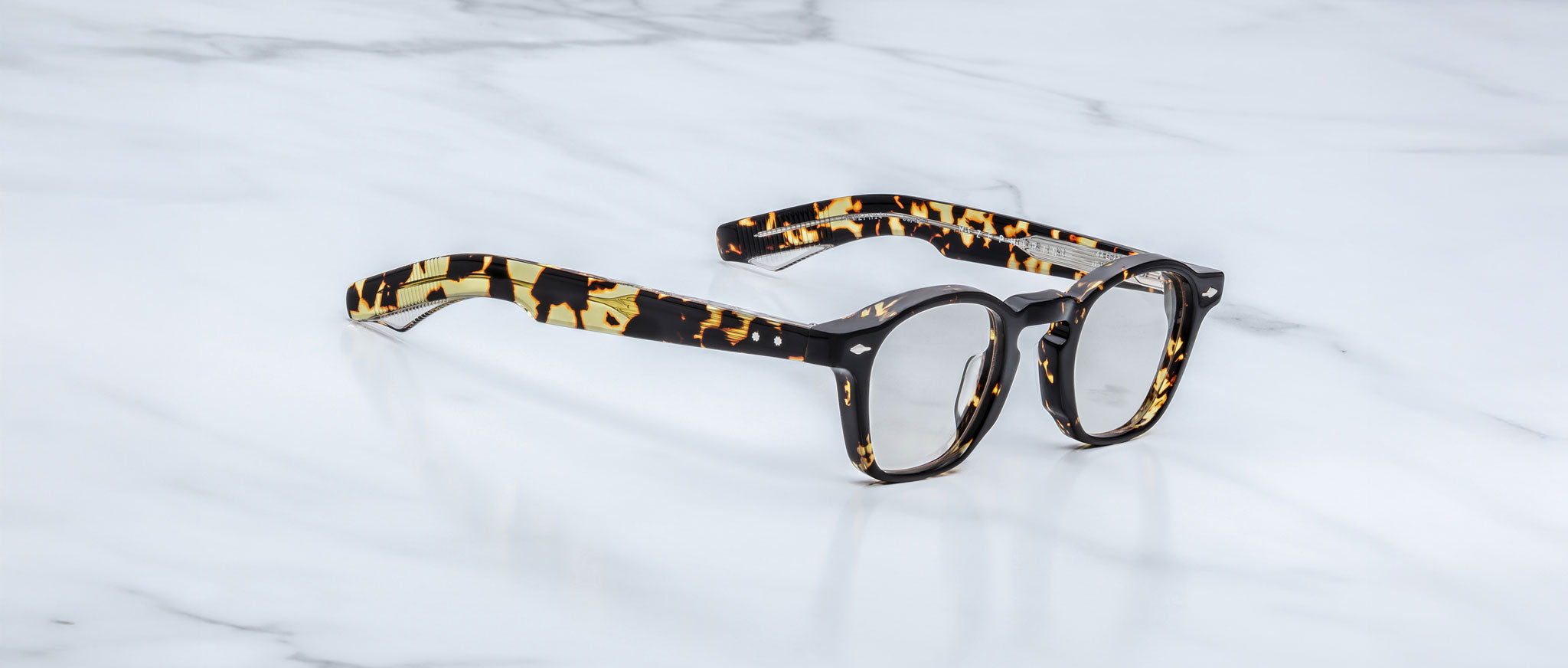 A pair of handcrafted Jacques Marie Mage Zephirin acetate spectacles rest elegantly on a white marble surface.