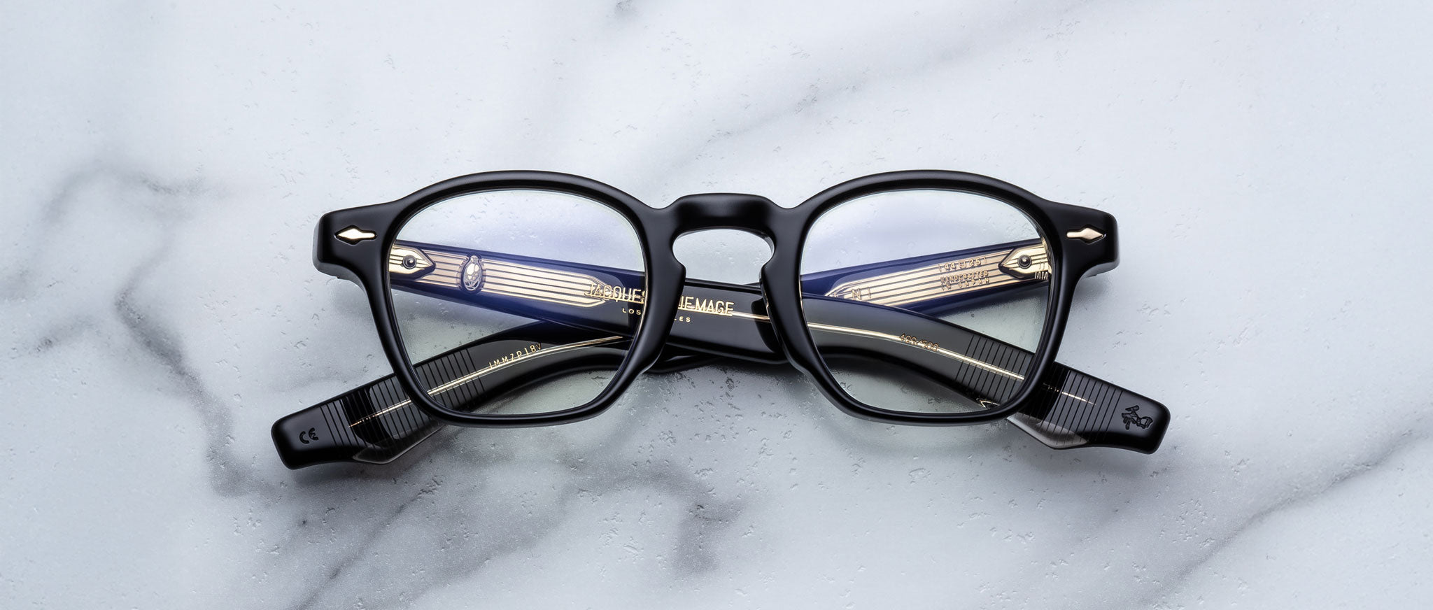 Jacques Marie Mage Zephirin black-framed eyeglasses, handcrafted from acetate with the brand name visible on the arms, elegantly displayed on a white marble surface.