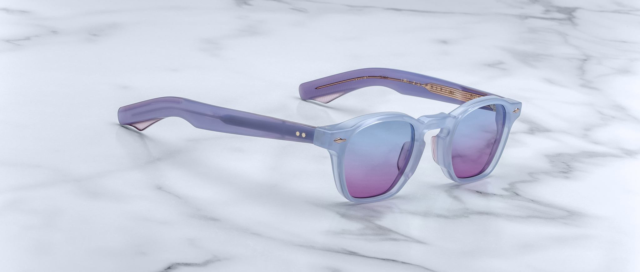 Jacques Marie Mage Zephirin sunglasses in light purple with tinted lenses are displayed on white marble—a striking, limited edition eyewear piece by Jacques Marie Mage.