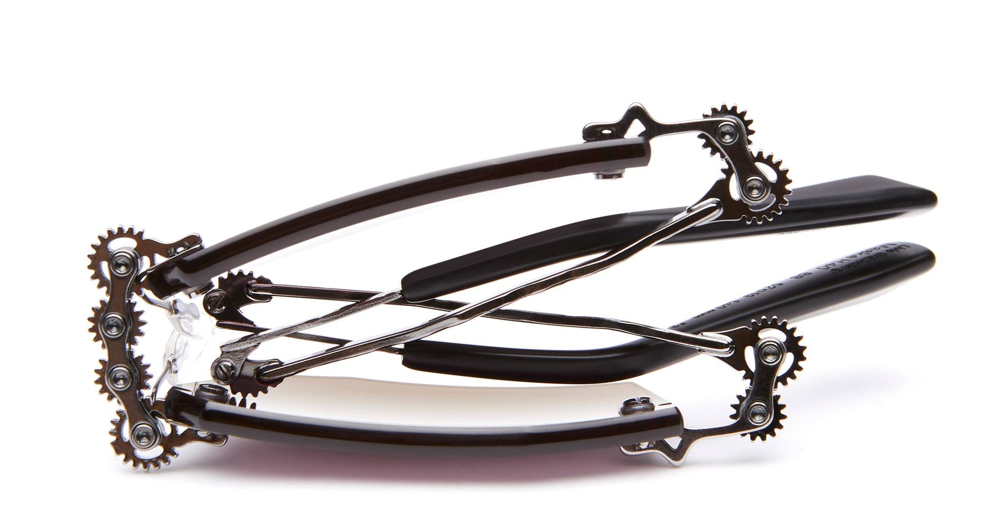 A metal nutcracker with black handles, viewed from the side, showing interlocking gears and wires that operate the cracking mechanism. The tool is positioned on a white background.