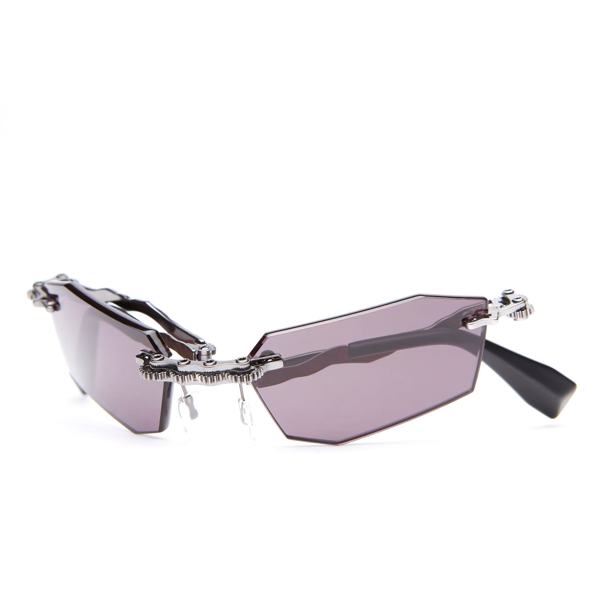 Futuristic sunglasses with angular, asymmetrical purple lenses, exposed metallic hinges, and black temples, displayed on a white background.