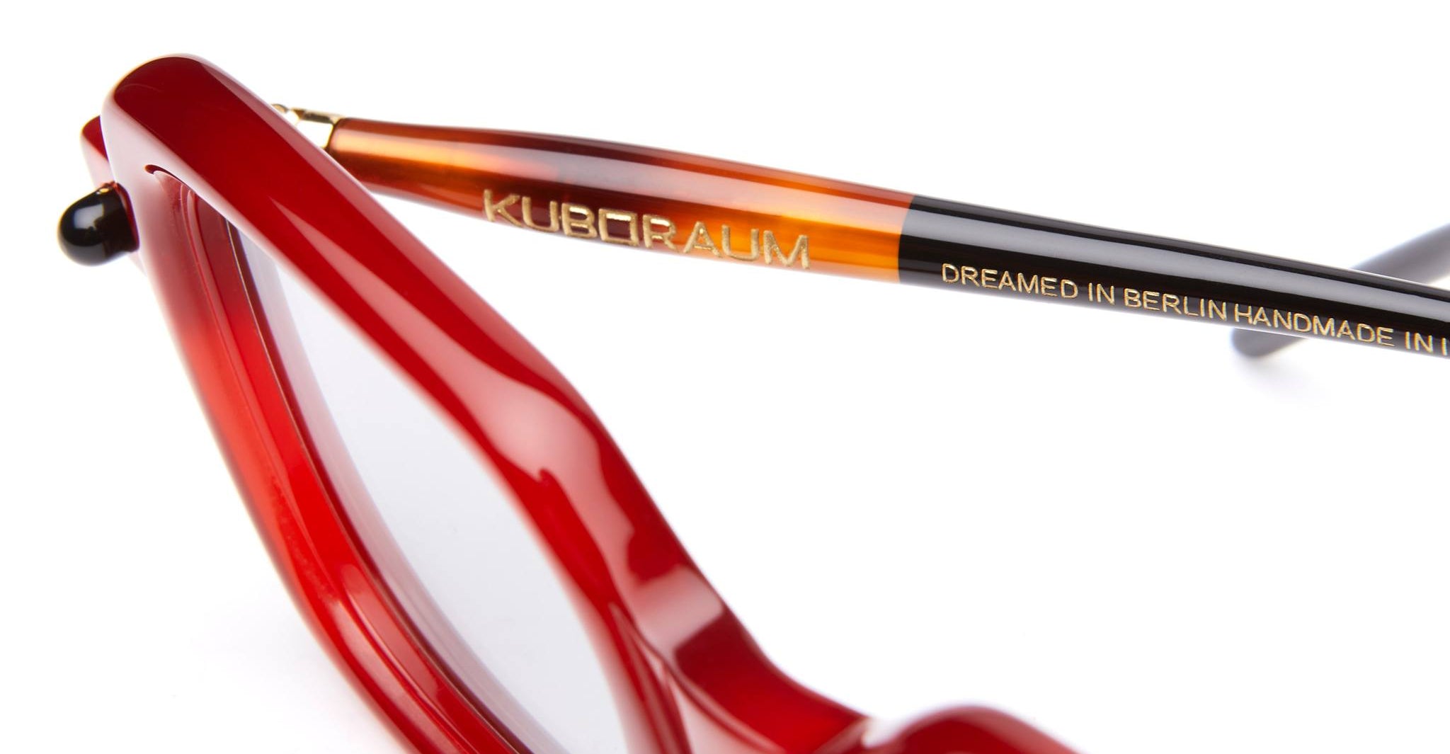 Close-up of red eyeglass frames with focus on the arm, which has the brand name Kuboraum and the text Dreamed in Berlin Handmade in... printed in gold.