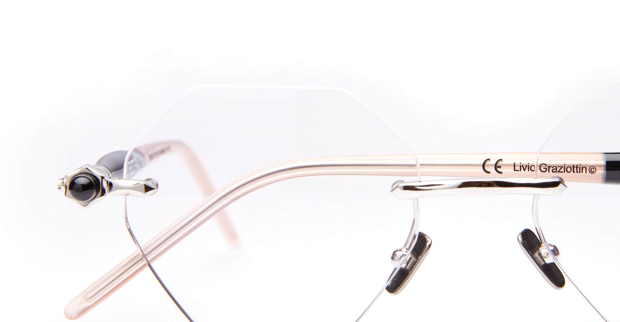 Close-up of rimless, geometric eyeglasses with transparent lenses and thin, light-colored arms against a white background. The brand name “Livio Grazottin” is visible on the arm.