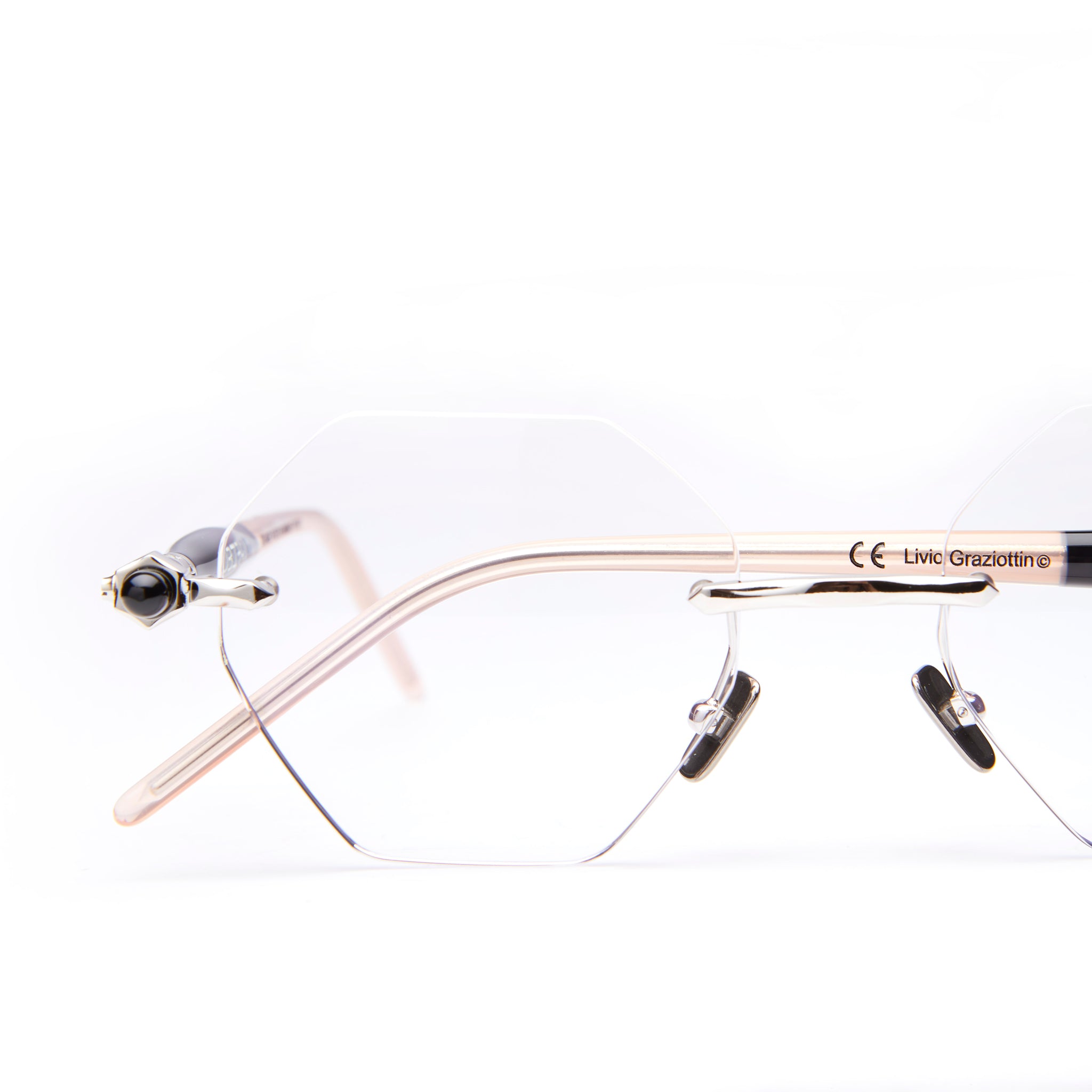 Close-up of rimless, geometric eyeglasses with transparent lenses and thin, light-colored arms against a white background. The brand name “Livio Grazottin” is visible on the arm.