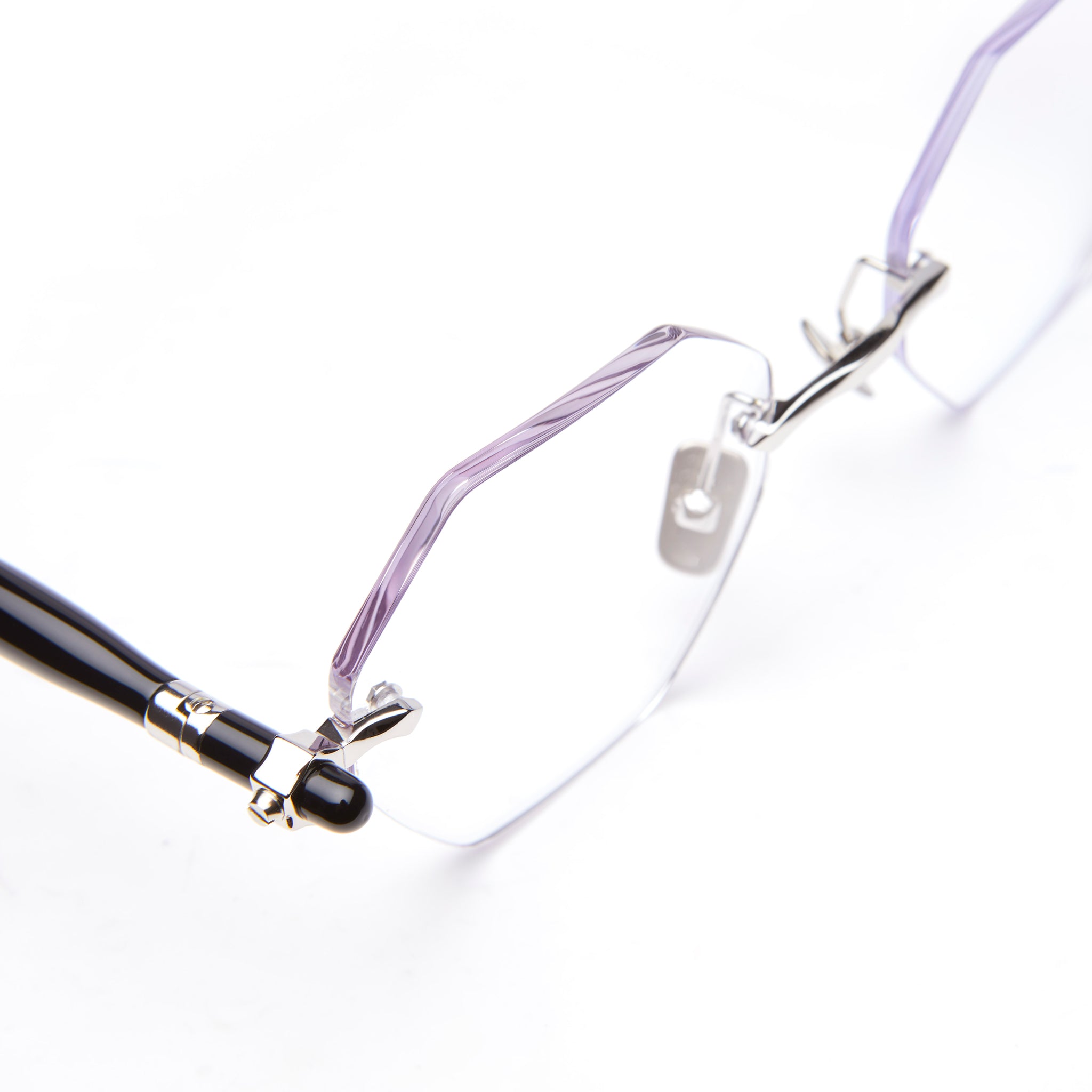 Close-up of rimless, hexagonal eyeglasses with thin metal bridge and black temple arms on a white background.