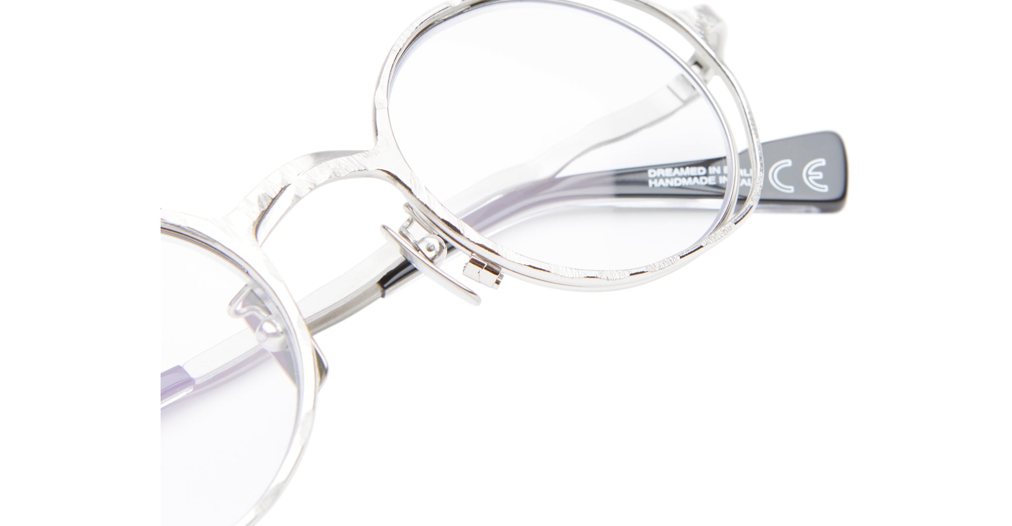 Close-up of Kuboraum H11 clear, round eyeglasses with silver hinges. The black arm displays printed text, including “CE” and “HANDMADE,” against a white background.