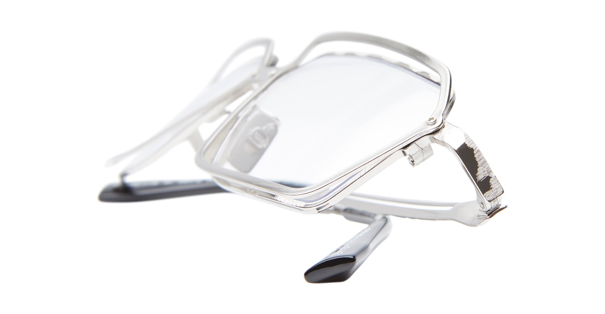 A pair of Kuboraum H15 silver rectangular eyeglasses with clear lenses sits folded on a white background, viewed from a low angle.