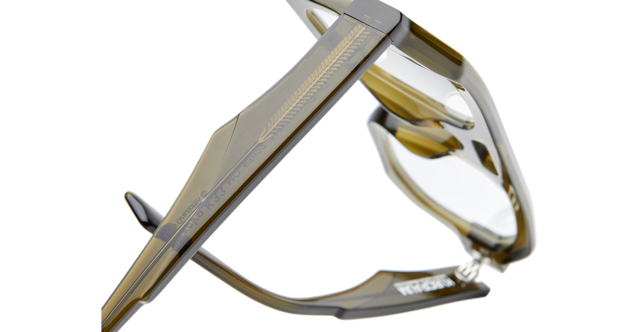 Close-up of translucent olive-green Kuboraum K33 eyeglass frames, featuring intricate etching along the temple and clear lenses. The brand name appears on the inside of the temple arm.