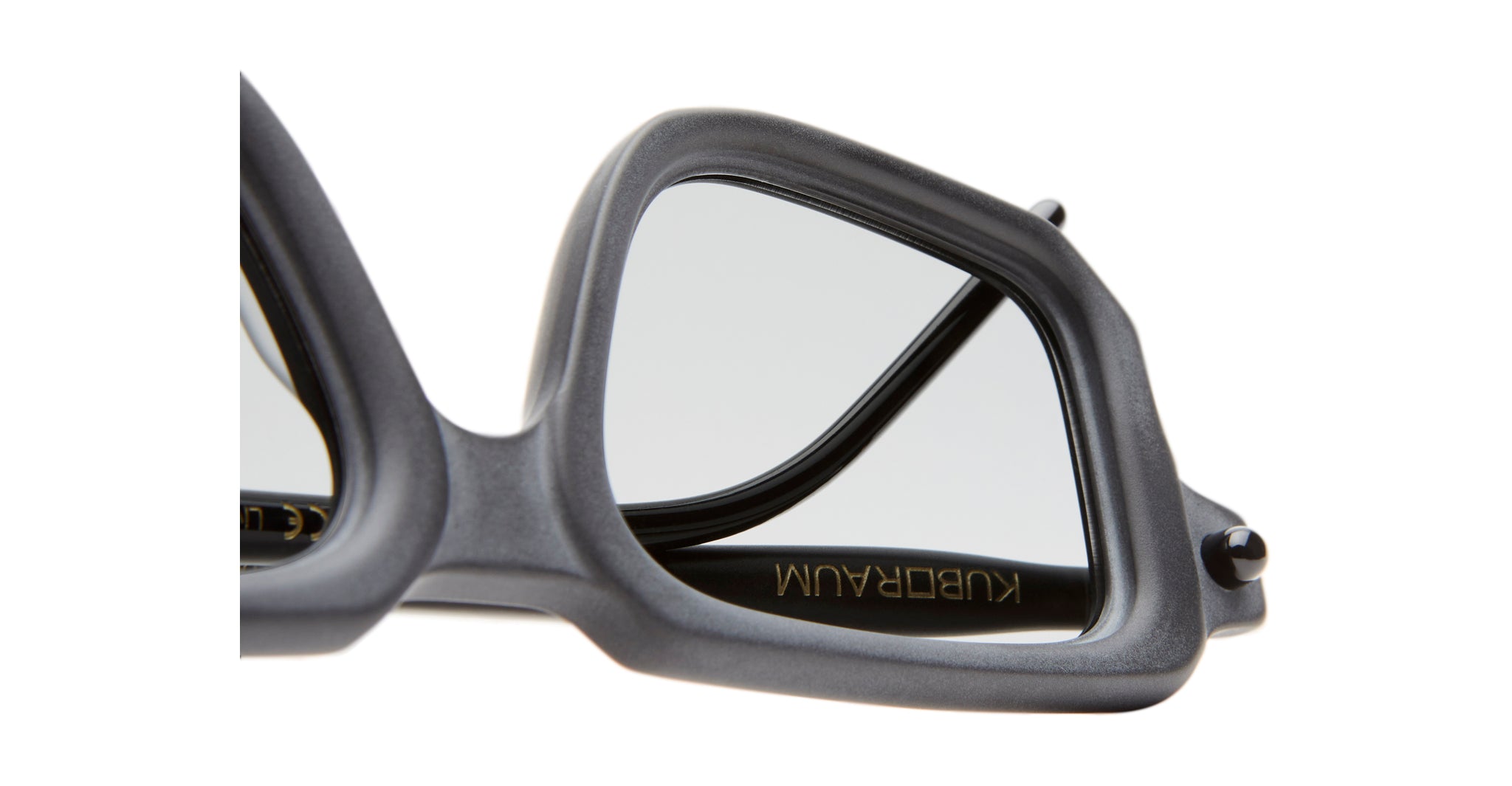 Close-up of Kuboraum P23 black angular sunglasses, highlighting part of the frame and lens with KUBORAUM in gold on the inside of the temple arm.