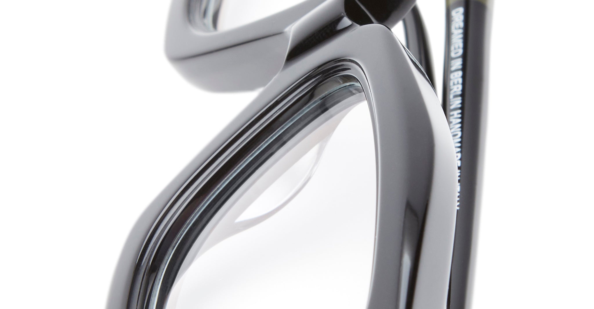 Close-up of the corner of Kuboraum P25 black eyeglasses with clear lenses, highlighting the glossy frame and part of a temple arm with small white text.