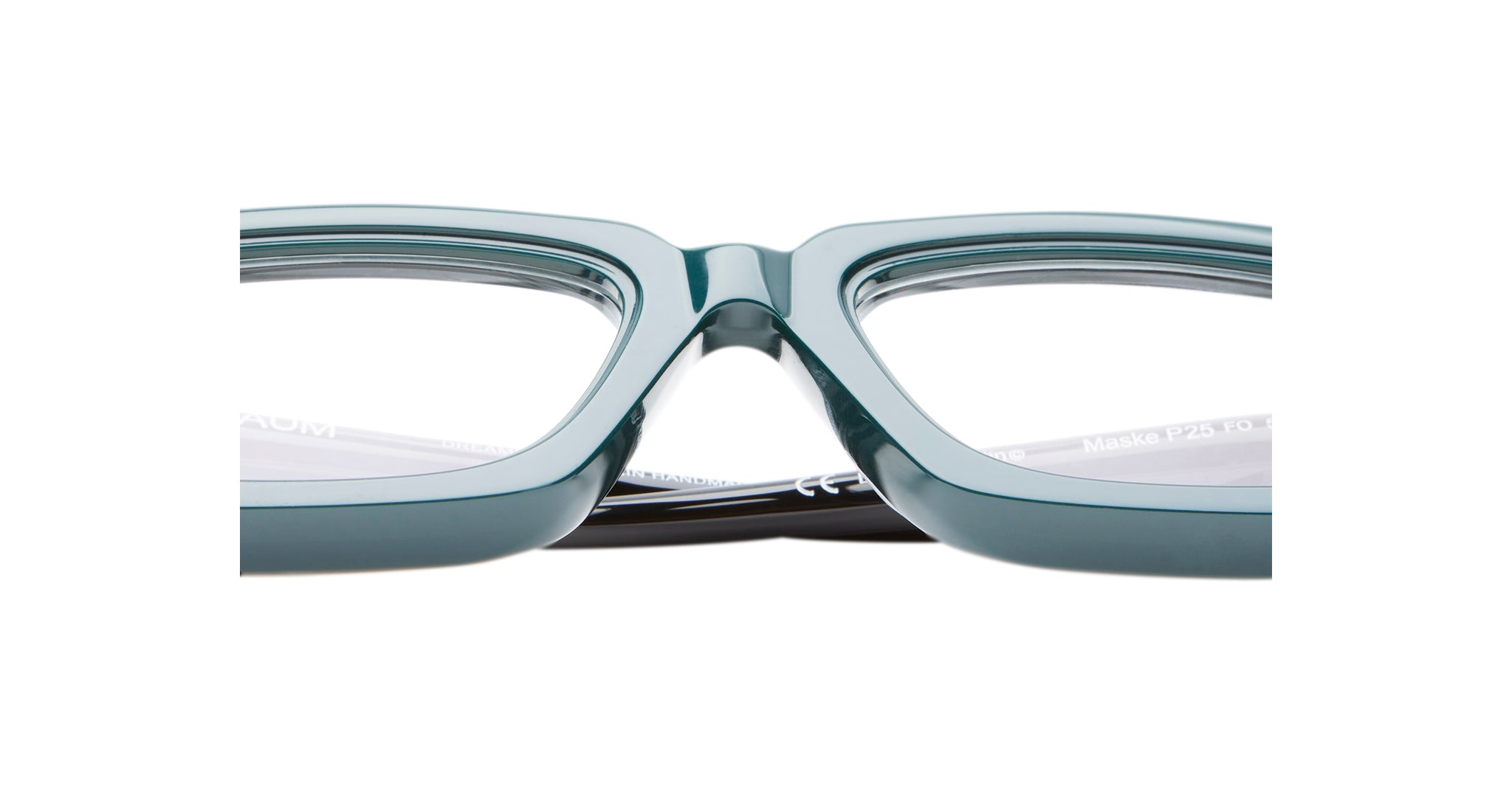 Close-up of the bridge and lenses of Kuboraum P25 teal rectangular eyeglass frames, highlighting their glossy finish and clear prescription lenses against a white background.