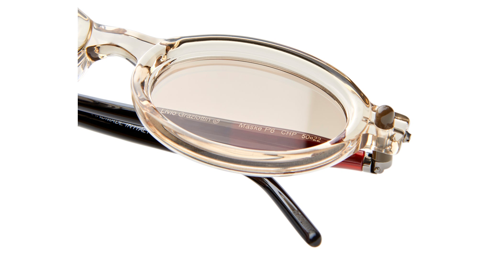 Close-up of Kuboraum P6 round eyeglasses featuring transparent beige frames, slightly tinted lenses, and visible black and red temple arms with text printed on the inner side.