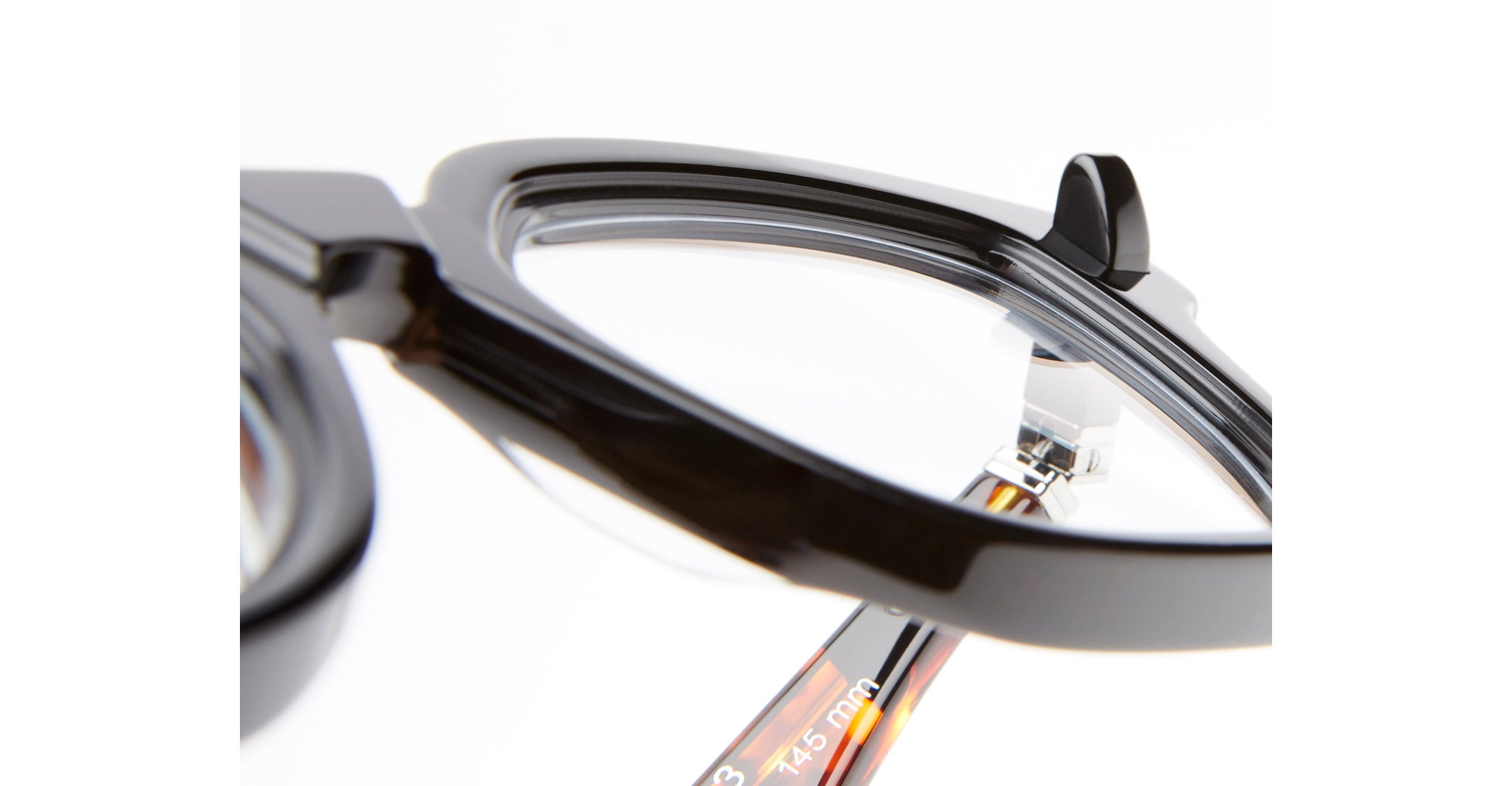 Close-up of the Kuboraum Q3 black eyeglasses’ corner, highlighting the glossy frame, clear lens, and part of the temple arm with measurement details visible against a white background.