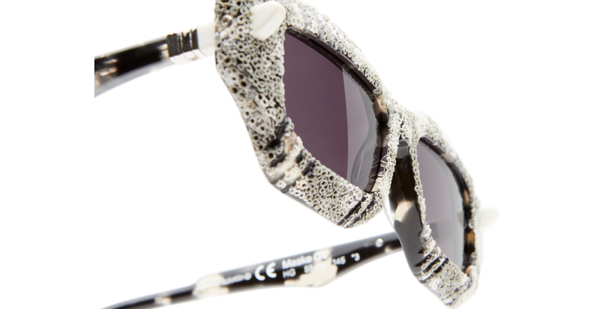 Close-up of Kuboraum Q6 sunglasses with black lenses and a textured light gray and black speckled frame featuring unique, irregular surface details, set against a white background.