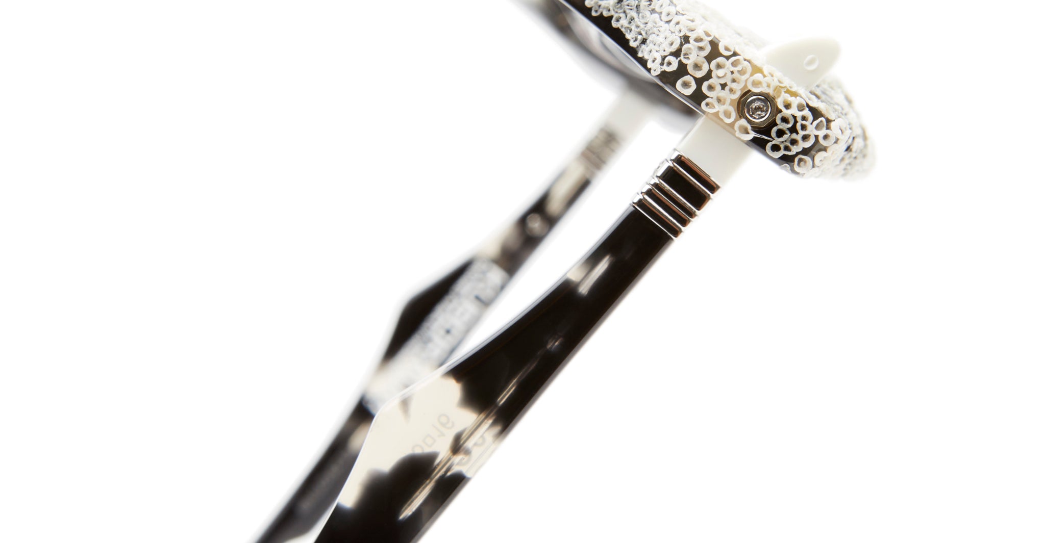 Close-up of Kuboraum Q6 eyeglass arms in a tortoiseshell pattern with a white frame, adorned with small white and silver beads, set against a white background.
