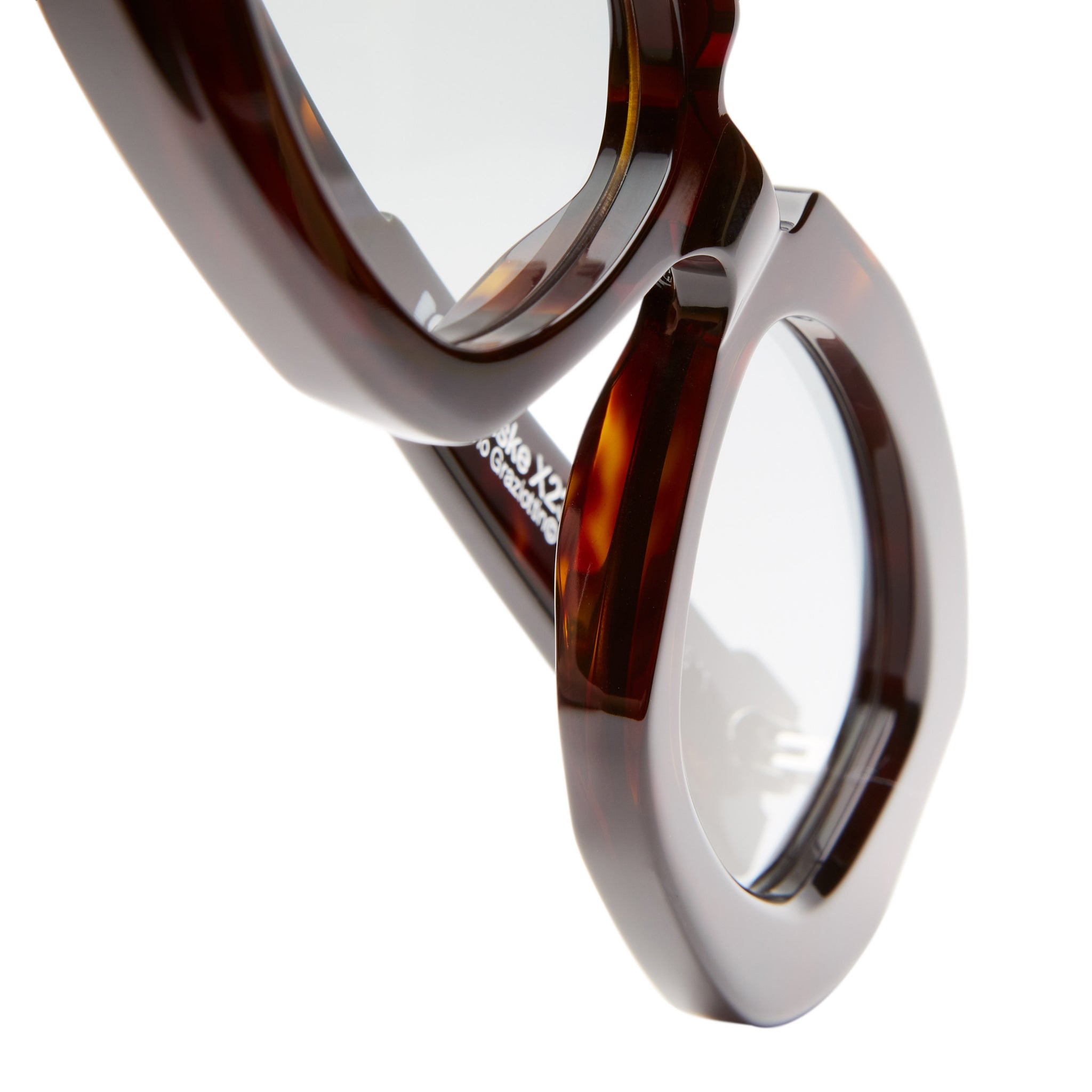 Close-up of Kuboraum X23 tortoiseshell round eyeglasses with transparent lenses on a white background, highlighting the frame and hinge details.