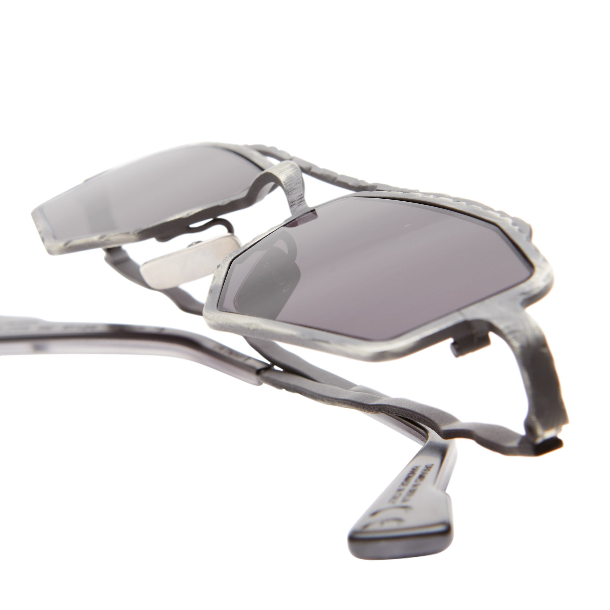 Close-up of Kuboraum Z23 sunglasses featuring geometric silver frames and dark tinted lenses, highlighting their unique angular design and metallic texture against a white background.