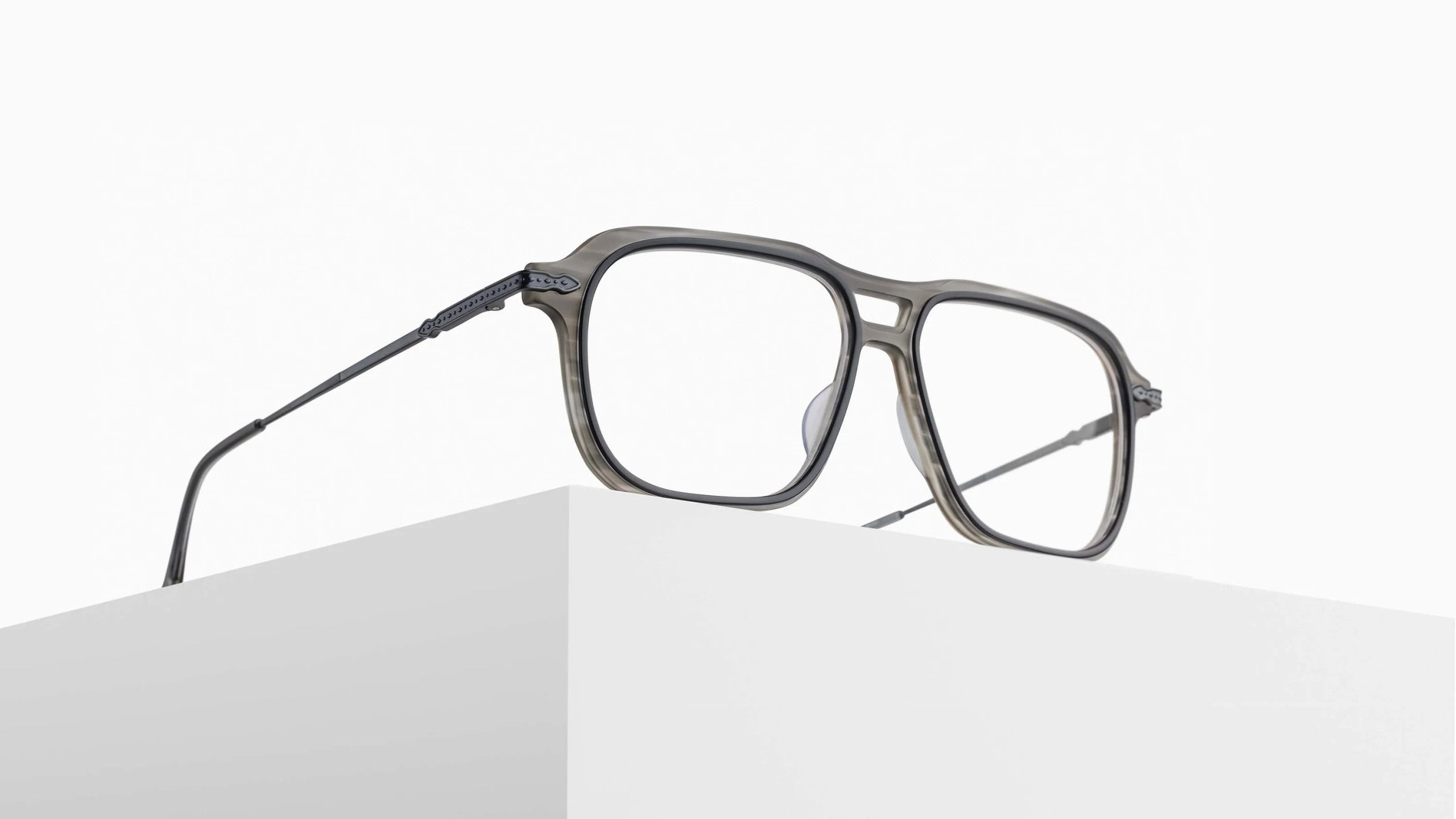 The Matsuda M2062, a pair of stylish eyeglasses with rectangular frames, rests on the edge of a white minimalist block against a plain white background.