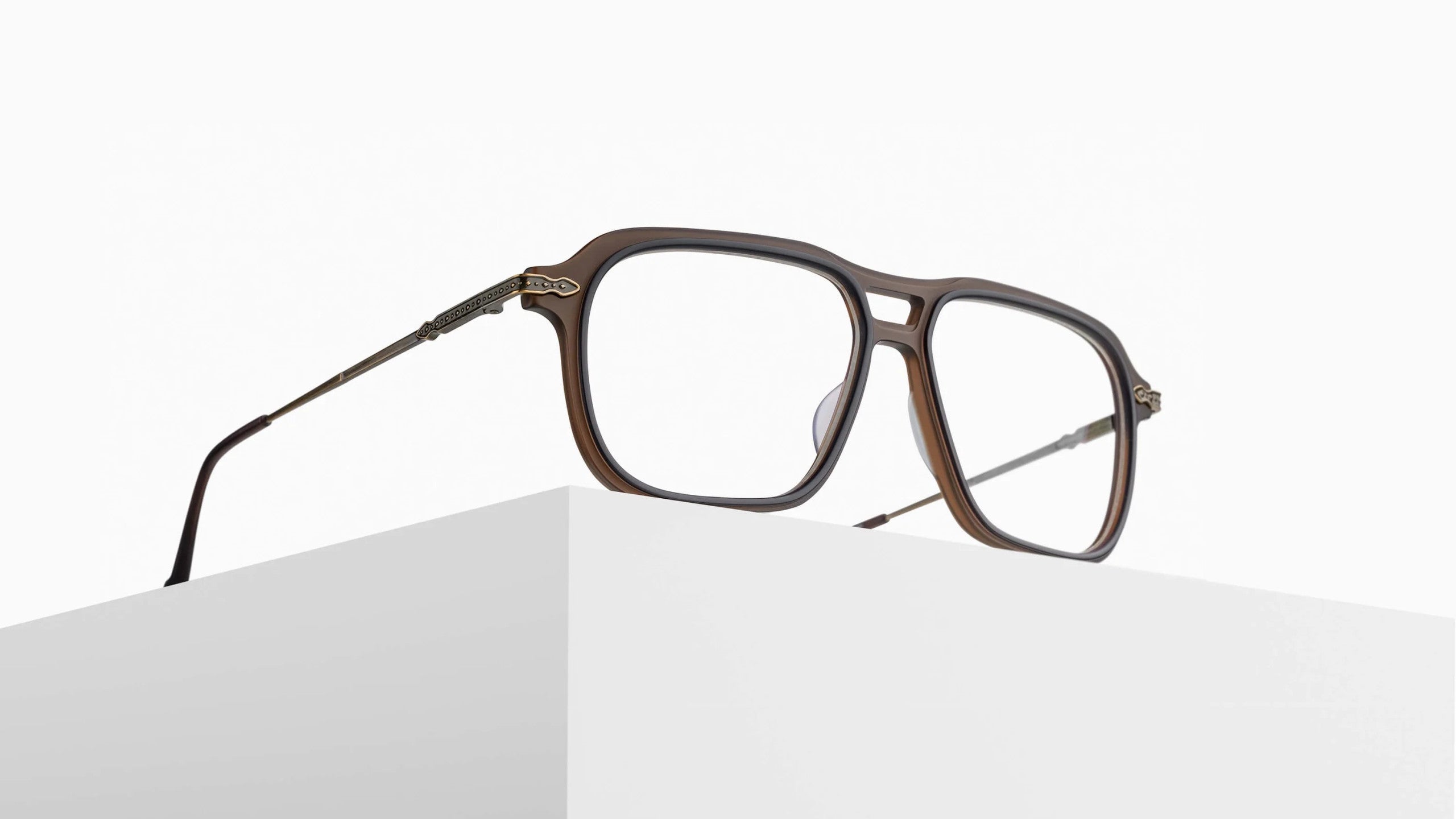 The Matsuda M2062 brown rectangular eyeglasses with metal arms are displayed on a white geometric pedestal against a plain white background.
