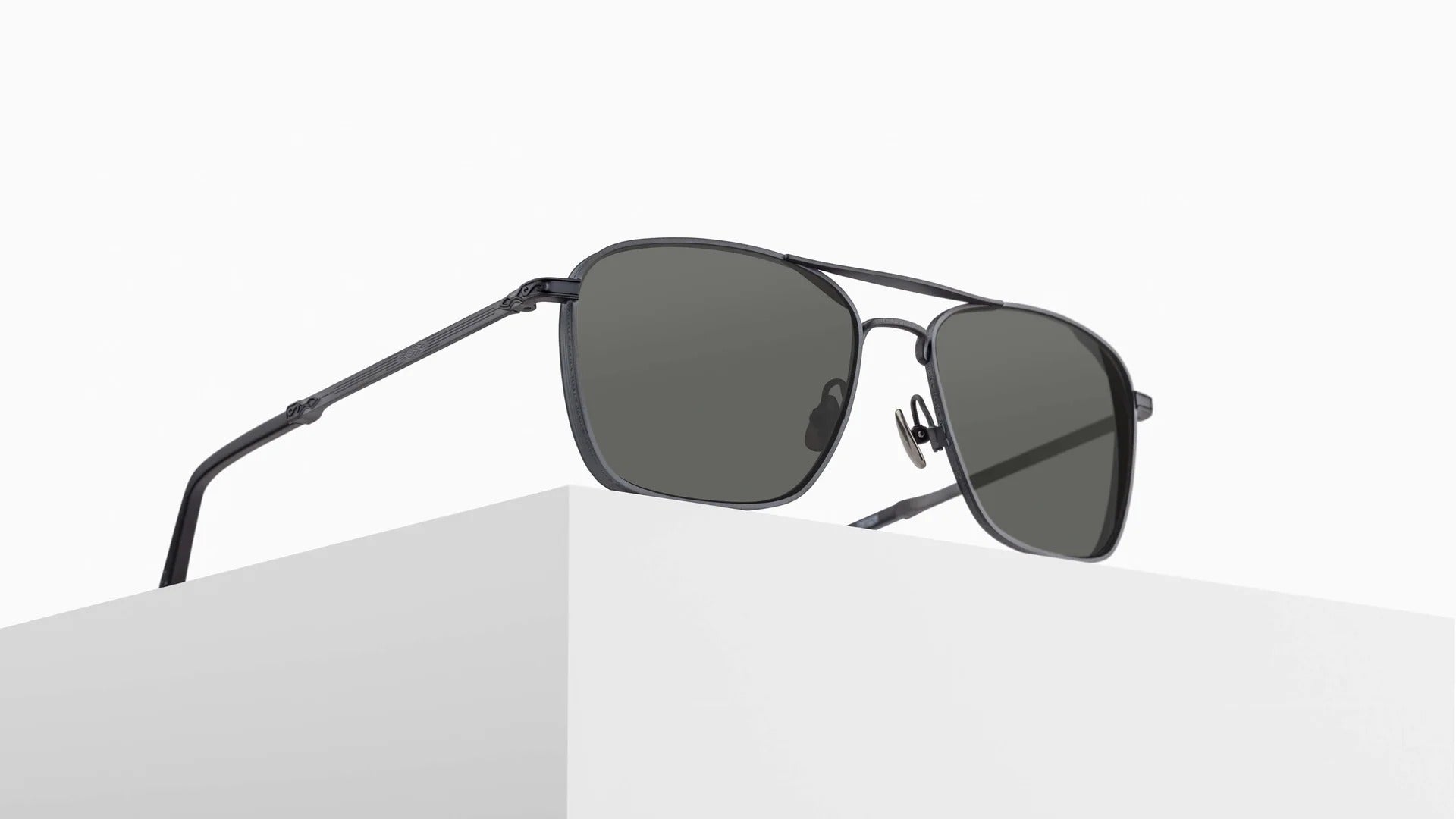 The Matsuda M3135 black aviator-style sunglasses with dark lenses are displayed on the edge of a white minimalist block against a plain white background.