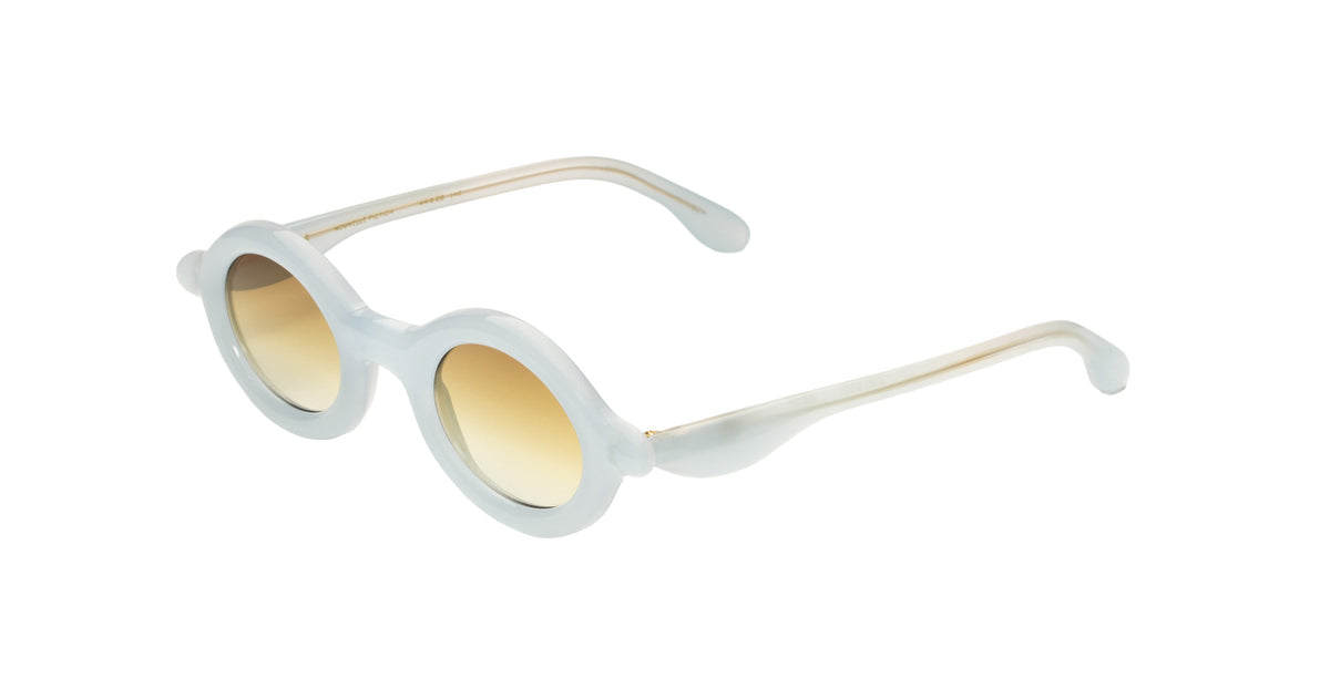 Paloceras Nouvelle Fiction R2 Milky Blue sunglasses in a pale translucent blue frame with thick rounded oval rims and warm golden gradient lenses, three-quarter view