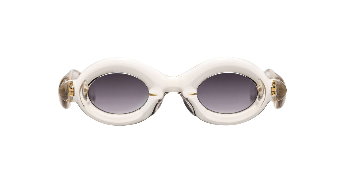 Paloceras Pebble RX Dulce Gloss sunglasses in a clear champagne frame with thick rounded oval rims, gray violet lenses, and gold-tone details, front view