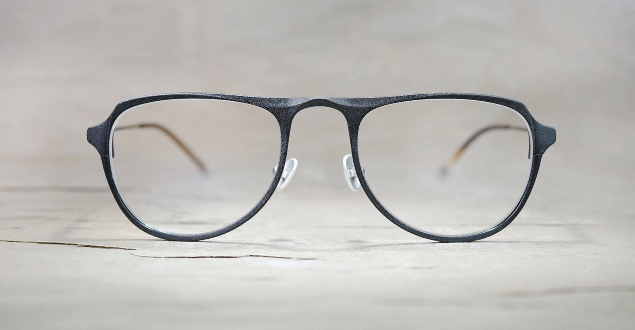 The Rigards RG0101AL, a pair of black, full-rimmed handcrafted eyewear with clear lenses, is displayed on a light textured surface and photographed from the front.