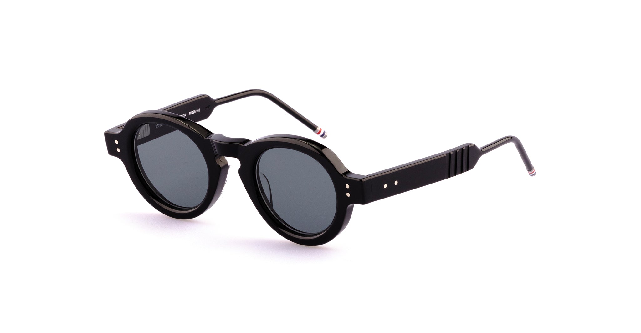 Thom Browne 922 black round-frame sunglasses with dark lenses, thick arms featuring small metallic accents, and subtle striped tips, shown on a white background.