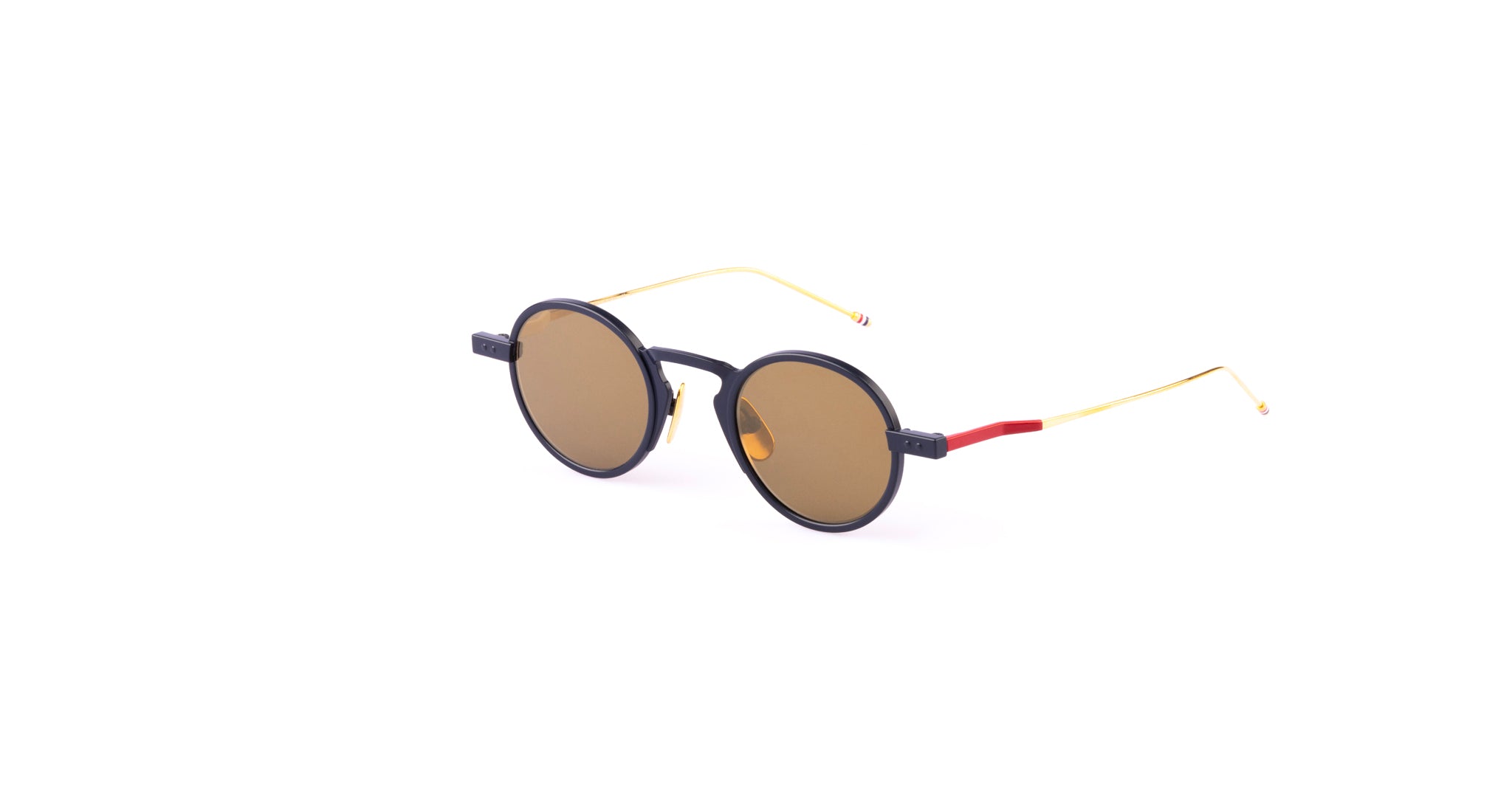 Thom Browne 931 luxury round sunglasses with dark lenses, a black frame, thin gold temples, and a red hinge accent are displayed diagonally on a plain white background.