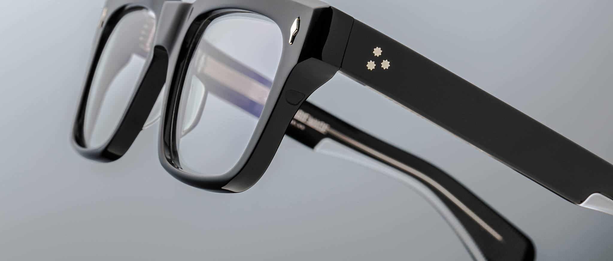 Close-up of Jacques Marie Mage Torino eyeglasses—bold rectangular frames in handcrafted acetate, clear lenses, and three small star-shaped accents on the temple, by Jacques Marie Mage.