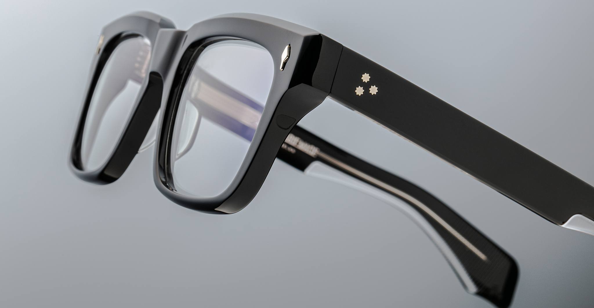 Close-up of Jacques Marie Mage Torino eyeglasses—bold rectangular frames in handcrafted acetate, clear lenses, and three small star-shaped accents on the temple, by Jacques Marie Mage.