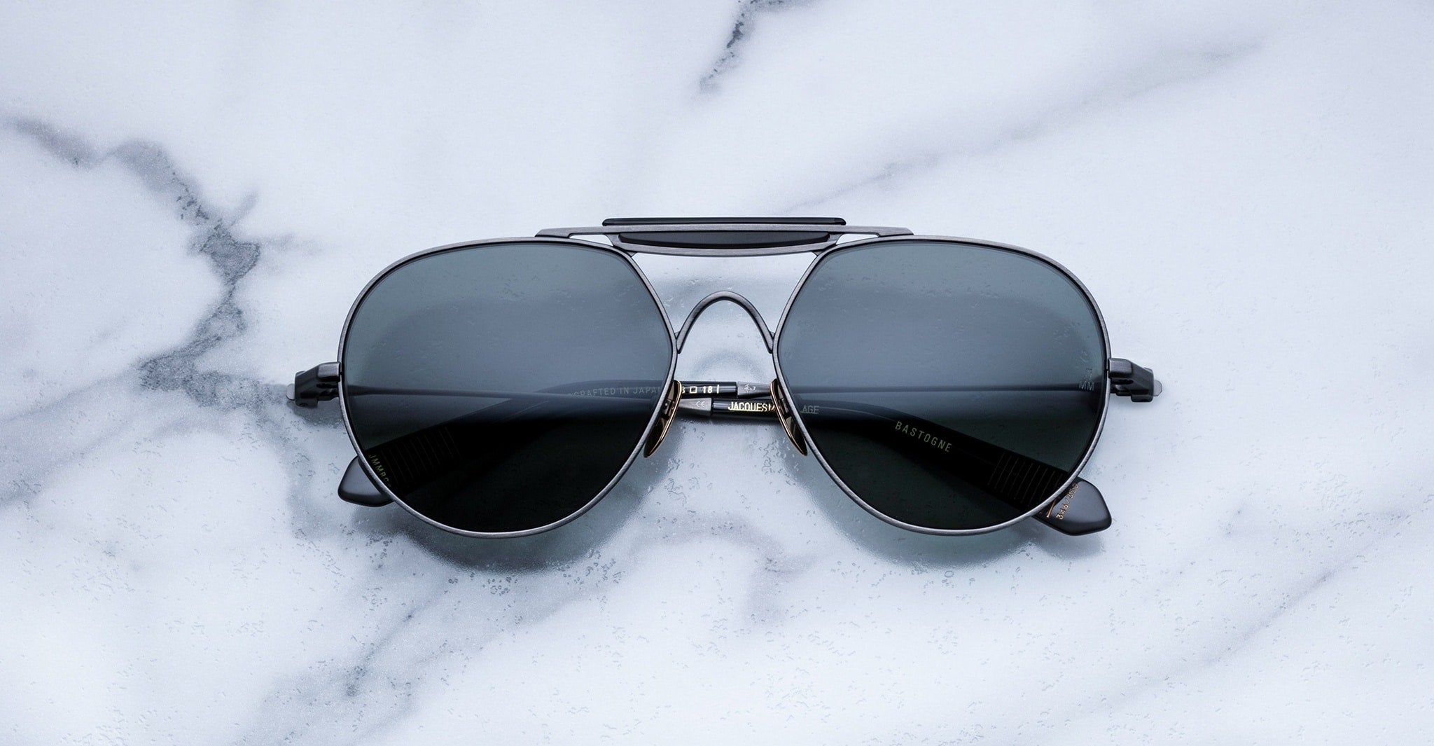 A pair of black aviator sunglasses with dark lenses lies on a white marble surface with gray veining.